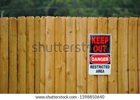 Keep out warning sign, alert danger and that it is a restricted area hanging on a wood fence.
