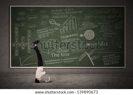 Businessman acrobatic move in classroom with business doodle on blackboard