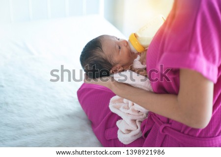 Asian mother feeding her baby boy with his bottle in the bedroom, Mom nursing new born baby