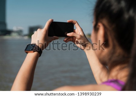 Athletic woman taking cityscape photo with phone from the park in a summer day