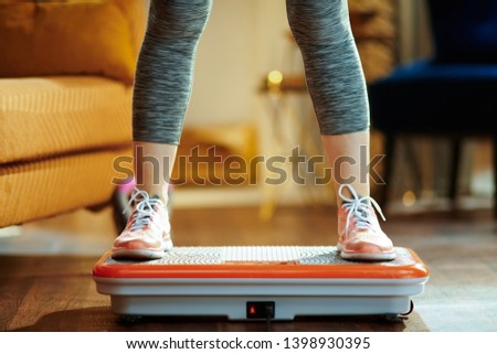 Closeup on young woman in fitness clothes in the modern house training using vibration power plate. Royalty-Free Stock Photo #1398930395