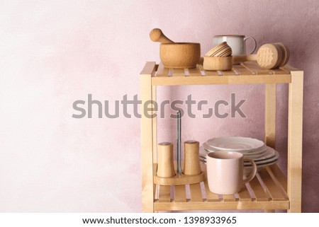 Wooden shelving unit with set of kitchenware near color wall. Space for text