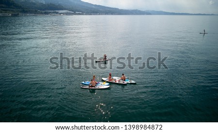 A company of five young people in bathing suits doing yoga and photographed on SAP surfing in the black sea, Sochi. Active rest on the water.