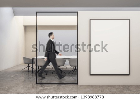 Side view of attractive european businessman walking in modern white meeting room interior with empty banner on wall. Worker concept. Mock up,