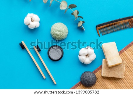 eco friendly bamboo tooth brush and carbon toothpaste, comb, organic soap on blue background top view