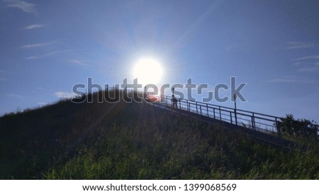 Long staircase leading to the top of the hill at sunset.  An iron staircase leads to the top of the mountain.  Stairs leading to the height.  Stairs uphill against the blue sky and the sun.