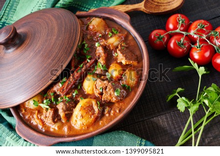 Traditional greek beef stew stifado or stifatho of a marinated cut of beef, red wine, onion, spices, cinnamon, tomato, served on a clay pot sprinkled with parsley, with a wooden spoon, close-up