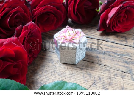 gift box with pink ribbon and red roses behind it at grunge wooden background. romance and concept.