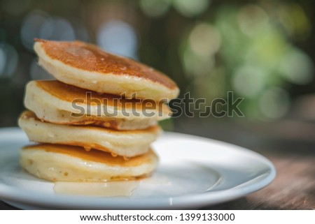 Stack of golden brown fluffy pancake on green bokeh background. The morning homemade snack is topped with fresh butter & hot maple syrup. It looks tasty but has lots of nutrition. Copy space given. 