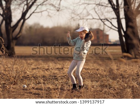 Little beautiful girl plays baseball in park on a warm sunny spring day