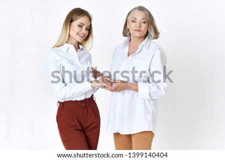 An elderly woman in a shirt holds the hand of a young daughter in red pants                          