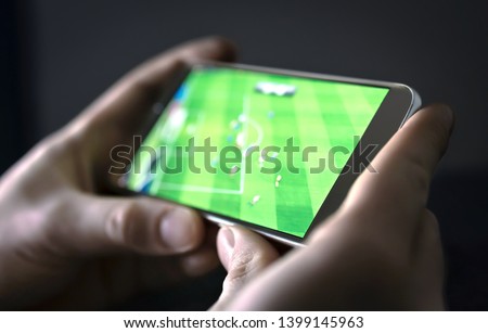 Watching football and sport stream with mobile phone. Man streaming soccer game live, video replay or highlights online with smart device. Sports fan and program of tv network in smartphone screen.  Royalty-Free Stock Photo #1399145963