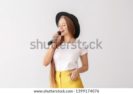 Beautiful female singer with microphone on light background Royalty-Free Stock Photo #1399174076