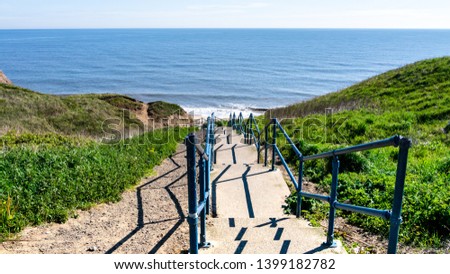 Concrete stairs leading down to Seaham Hall Beach in County Durham, England UK.  Image taken on a warm sunny day showing a calm North Sea, grass hills either side and a blue sky. Royalty-Free Stock Photo #1399182782