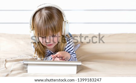 Focused little child using laptop with headphones studying  e-learning.