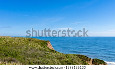 Cliff edge at Seaham Hall Beach in County Durham showing green grass at the edge of a cliff outlooking a calm North Sea.  Image taken on a warm sunny day. Royalty-Free Stock Photo #1399186133