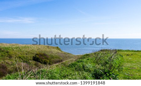 Edge of a cliff at Seaham Hall Beach in County Durham showing lush green grass outlooking a calm North Sea. Royalty-Free Stock Photo #1399191848