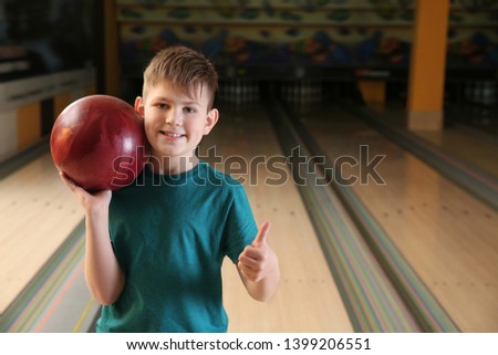 Little boy with ball showing thumb-up in bowling club