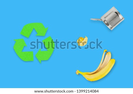 Symbol of eco recycling cut out of green paper near different garbage, banana peel, metal can, crumpled paper ball. Top view. Concept of save planet