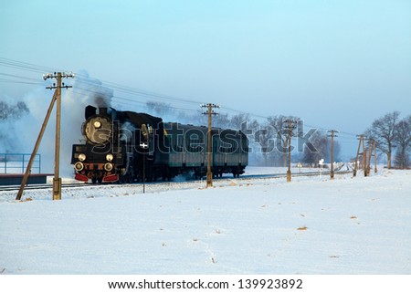 Vintage steam train puffing through countryside during wintertime 