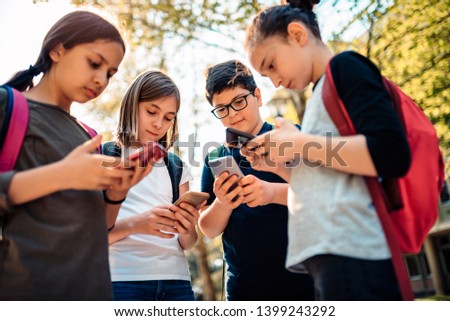 Group of school kids hang out in schoolyard and using smart phone Royalty-Free Stock Photo #1399243292