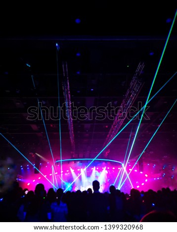 Blurred crowd at concert : Silhouette people crowd happy and cheering in front of colorful stage with bright laser light beam. Music superstar performance. Soft focus