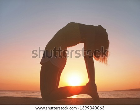 Silhouette of woman in pose of half-bridge on beach. Freedom and harmony concept. Girl is doing yoga against sunset.  - Image 