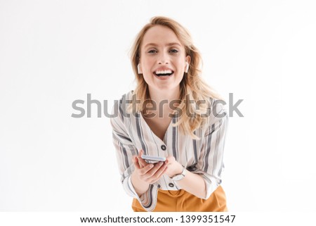 Photo of young smiling woman wearing wrist watch using cellphone and earpods isolated over white background in studio