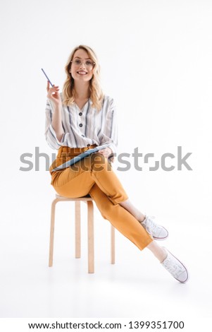 Photo of caucasian cute woman wearing glasses sitting in chair and holding clipboard isolated over white background in studio