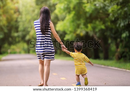 mother holds the hand of a small child walking at the park in sunny day.
