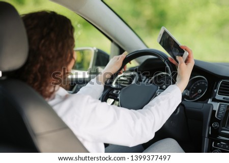 Smiling young woman taking selfie picture with smart phone camera while driving a car.