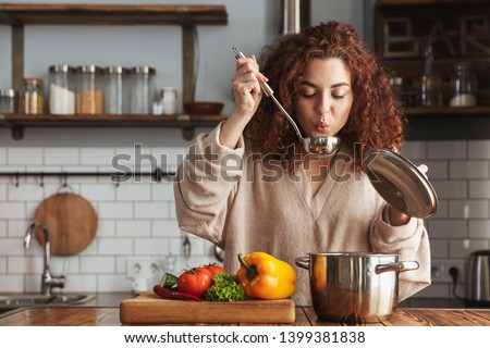 Photo of pretty caucasian woman holding cooking ladle spoon while eating soup with fresh vegetables in kitchen at home Royalty-Free Stock Photo #1399381838