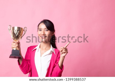 Successful young asian woman holding a trophy point to blank space on pink background