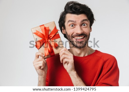 Image of a handsome young excited man posing isolated over white wall background holding present gift box.