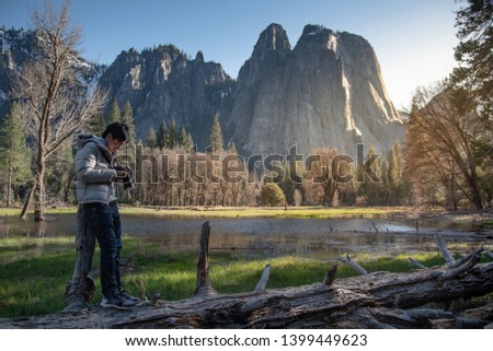 Asian man photographer and tourist holding DSLR camera taking photo of Cathedral Rock landscape in Yosemite National Park, famous natural attraction in California, USA. Travel photography concept