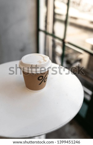 Close up composition of paper hot coffee cup on white metal table setting near glass window in natural light scene / coffee shop concept / nice composition background / background for advertising