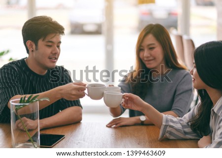 Close up image of three asian people enjoyed drinking and clinking coffee cups on wooden table in cafe
