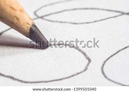 Close-up of a pencil with the tip and graphite mine flowing over the surface of a white sheet of paper drawing doodles and sketches