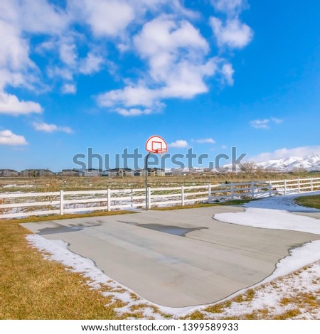 Clear Square Basketball court surrounded by a snowy and grassy terrain on a sunny winter day