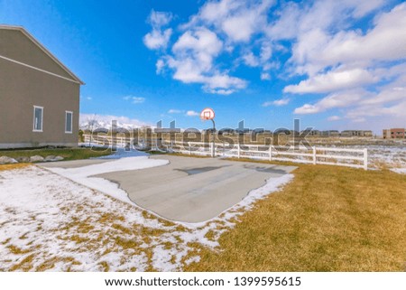 Basketball court surrounded by a snowy and grassy terrain on a sunny winter day