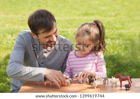 Cute toddler girl and dad play with farm animal figures outdoors. Summer vacation childhood in the countryside. The child learns farm animals. Early education and development