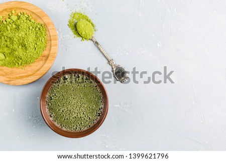 Matcha green tea in a brown Cup. The powder lies on a bamboo plate with a spoon. The background is light with copy space. Top view