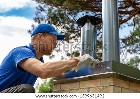 worker on the roof installing tin cap on the brick chimney Royalty-Free Stock Photo #1399631492