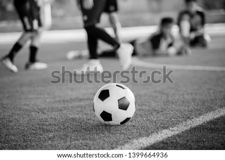 Black and white picture of Soccer ball on green artificial turf with blurry of maker cones and player training. Soccer academy