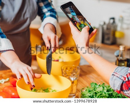 Cooking blog. Two women making salad cutting vegetables taking smartphone pictures. Healthy nutrition vegan lifestyle.