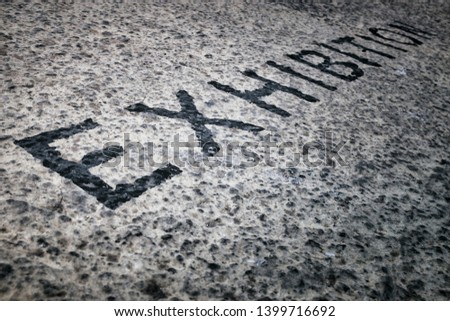 "EXHIBITION" written on asphalt or concrete wall, sign written in black letters