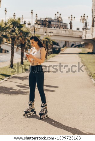 Cute girl rollerblading outdoors while looking at her phone on a sunny day close to the river