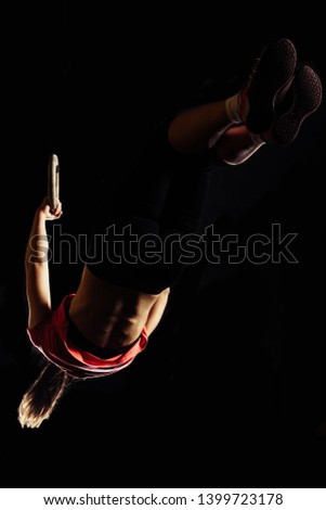 Fit young girl in the black sportwear exercising with gymnastic rings in gym, low key dark image