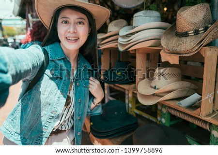 Beautiful asian woman taking selfie buying hats at olvera street vendor. Consumerism shopping traveling lifestyle concept. young girl tourist make self photo wearing straw hat in local mexico market