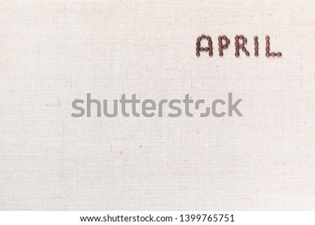 The word April written with coffee beans on creamy linea canvas, shot from above, aligned at the top right.